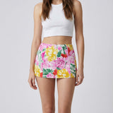 Woman wearing a white crop top and colorful floral skirt on a plain background